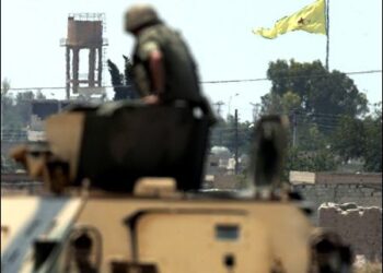 Turkish soldier looking at Kurdish flag in Gire Spi (Tel Abyad), Syrian Kurdistan