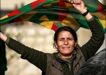 A Kurdish woman dances with a Kurdistan flag in Rojava