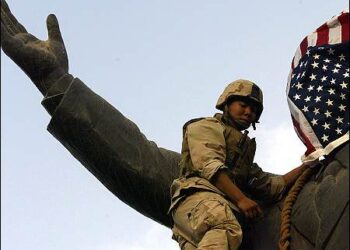 A U.S. Marine covers the face of a statue of Iraqi President Saddam Hussein with a U.S. flag in Baghdad, on April 9, 2003. Photo: Reuters
