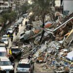 Lebanese motorists, some waving Hezbollah flags, drive past a ruined building in Beirut