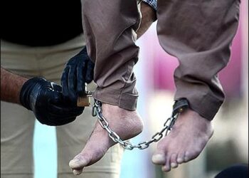 A Iranian hangman removes chains from the legs of a dead man who has been publicly hanged