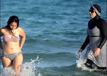 Two women walking through the sea, one wearing an Islamic burkini (right), the other in a bikini. Photo: AFP