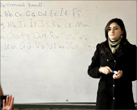 A Kurdish language teacher stands in front of a whiteboard in a classroom in the town of Rumeilan, Syrian Kurdistan, Rojava